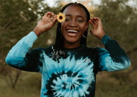 Young happy woman wearing a tie-dye long-sleeve shirt holding a flower